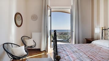 A bedroom with a bed, two chairs, a view to the outside, and a window with curtains.