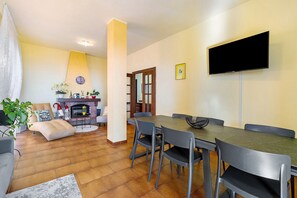 A dining area with a table and chairs, a flat-screen TV mounted on the wall, a fireplace, and a plant.