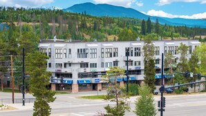 A multi-story building with a commercial ground floor, surrounded by trees and a mountain in the background.