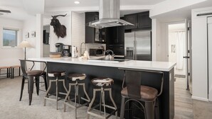 A modern kitchen with a central island, bar stools, and a mounted animal head.