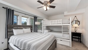 A bedroom with a single bed, a bunk bed, a ceiling fan, a bedside lamp, and a view of the outdoors through a window.