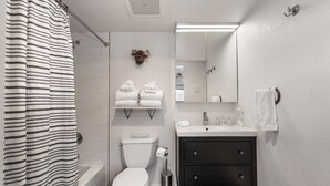 A modern bathroom with a striped shower curtain, a toilet, a sink with a mirror, and a decorative moose head on the wall.