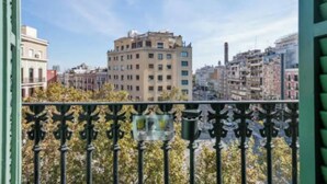 Een balkon met decoratieve ijzeren hekwerk, met uitzicht op een stadsgezicht met meerlaagse gebouwen.