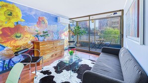 A modern living room with a glass coffee table, a sofa, a chair, a wooden cabinet, and a large flower mural on the wall. - Urban Bloom 3D, Wifi y Estacionamiento (Ñuñoa)