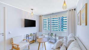 A modern living room with a sofa, chairs, a coffee table, a TV, and a large window with a city view. - Vista Infinita (Concón)