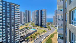 A high-rise residential building with multiple balconies, a swimming pool, and a road with cars. - Vista Infinita (Concón)