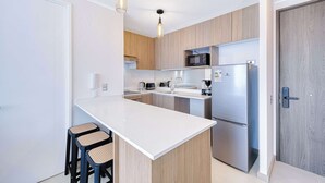 A modern kitchen with a central island, bar stools, a microwave, a refrigerator, and wooden cabinets. - Vista Infinita (Concón)