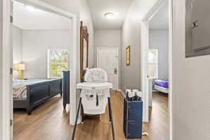 A room with a bed, a white high chair, a blue storage bin, and a door leading to another room.