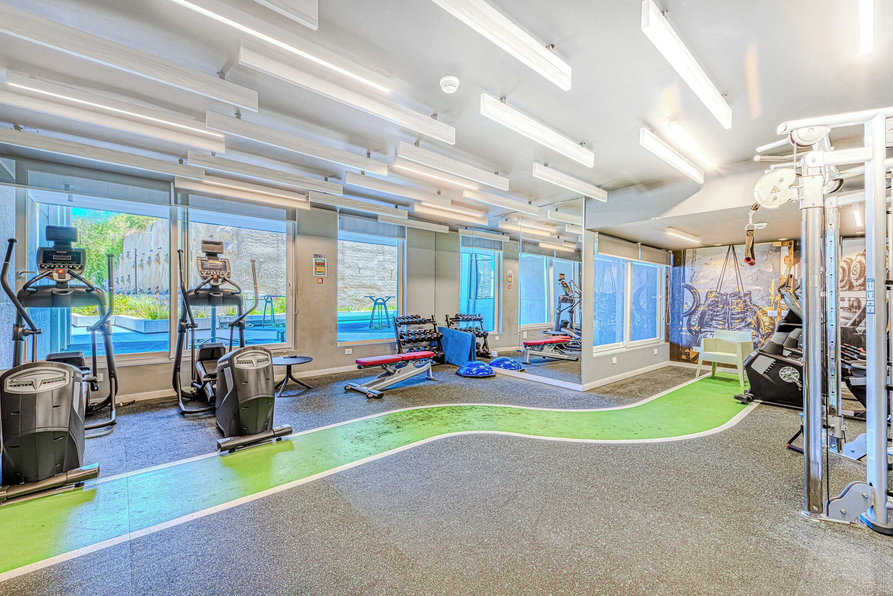 Une salle de sport moderne équipée de machines de cardio, d’appareils de musculation et dotée d’un tapis vert.