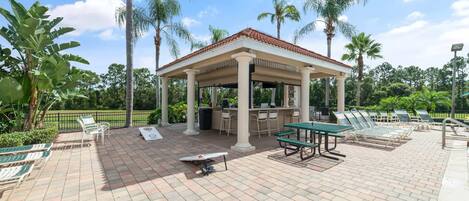 Un espacio al aire libre techado con una pérgola, sillones de descanso y una mesa.