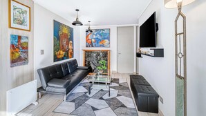 Una sala moderna con un sofá de cuero negro, una mesa de centro de vidrio, una chimenea y un televisor de pantalla plana montado en la pared.
