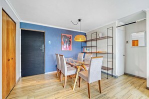 Een kamer met een eettafel, stoelen, een hanglamp, een boekenkast en een deur.