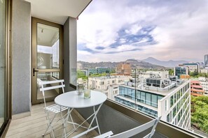 Ein Balkon mit weißem Tisch und Stühlen, der Blick auf die Stadt mit Gebäuden und einem Berg im Hintergrund bietet.
