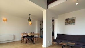 A spacious living area with a wooden floor, a dining table with chairs, a dark sofa, and a painting on the wall. - Beachfront Apartment w/ Balcony & Sea Views (Valras-Plage)