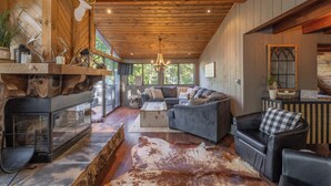 A cozy living room with a fireplace, leather sofas, and a large window offering a view of the outdoors.