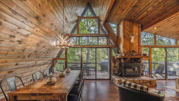 A wooden interior with a dining area, large windows, and a fireplace.