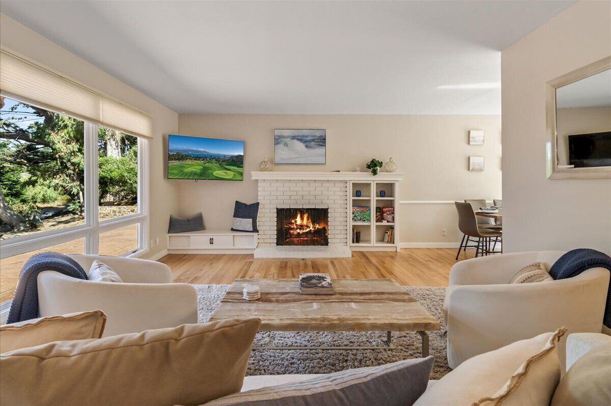A modern living room with a fireplace, comfortable seating, a television, and a view of the outdoors.