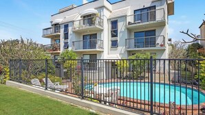 Un edificio residenziale a più piani con balconi, una piscina e un giardino recintato.