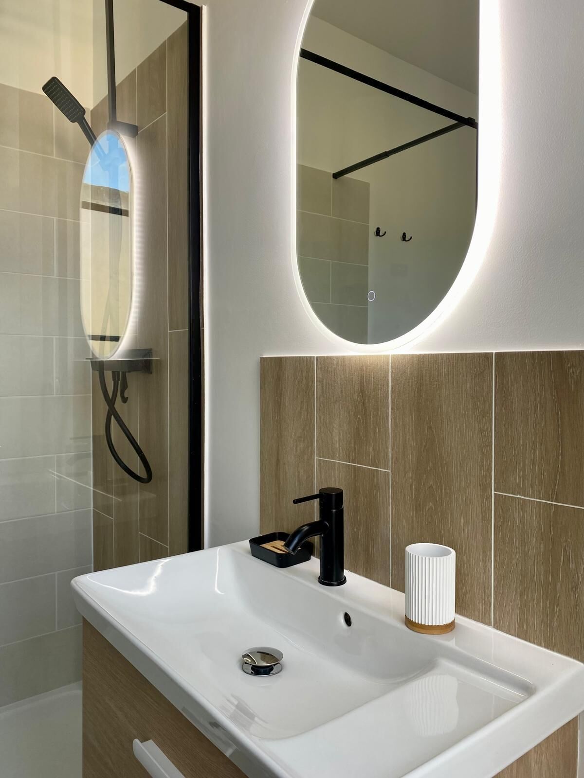 A modern bathroom with a white sink, black faucet, and a mirror with a light.