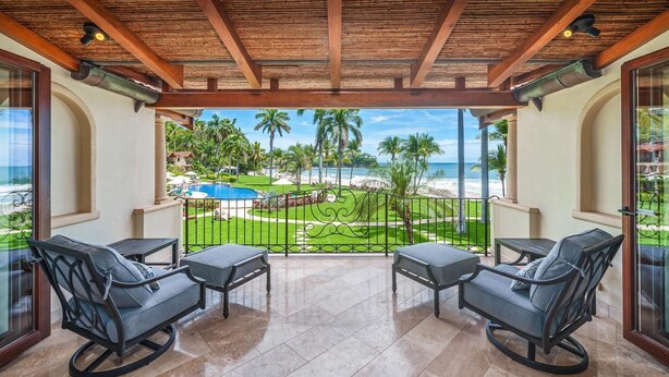 A balcony with two rocking chairs, a pool, and a view of the beach and palm trees.