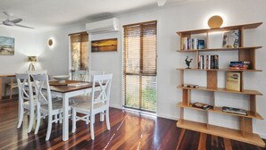 Un comedor con una mesa de madera y sillas blancas, una estantería y un ventilador de techo.
