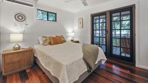 Un dormitorio con cama, mesitas de noche, ventilador de techo, ventana y puerta que da a un área exterior.