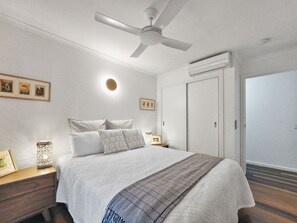 Une chambre à coucher comprenant un lit, un ventilateur de plafond, une table de chevet et une armoire.