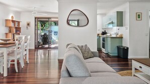 Una sala moderna con un sofá, un comedor con sillas y una mesa, una cocina con armarios, y un espejo grande en la pared.