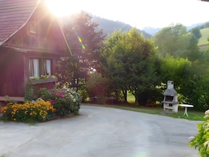 A rustic wooden house with a garden, a barbecue grill, and a bench.