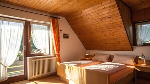 A bedroom with a sloped ceiling, a bed, a nightstand, and a window with curtains.