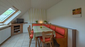 A dining area with a table, chairs, a bench, a television, and a window.