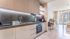 A modern kitchen with a built-in oven, a coffee machine, and a dining area with a table and chairs. - Furnished Studio with Burj Khalifa View, Near Dubai Water Canal (Dubai)
