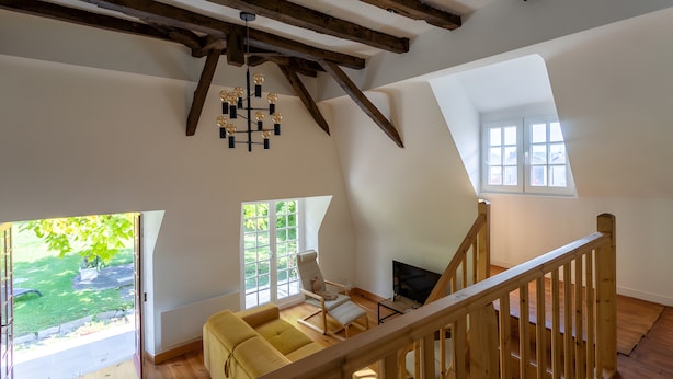 Un loft amplio con vigas de madera a la vista, un gran ventanal, un sofá amarillo y una escalera.