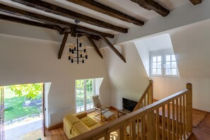 Un loft spacieux avec des poutres apparentes, une grande fenêtre, un canapé jaune et un escalier.