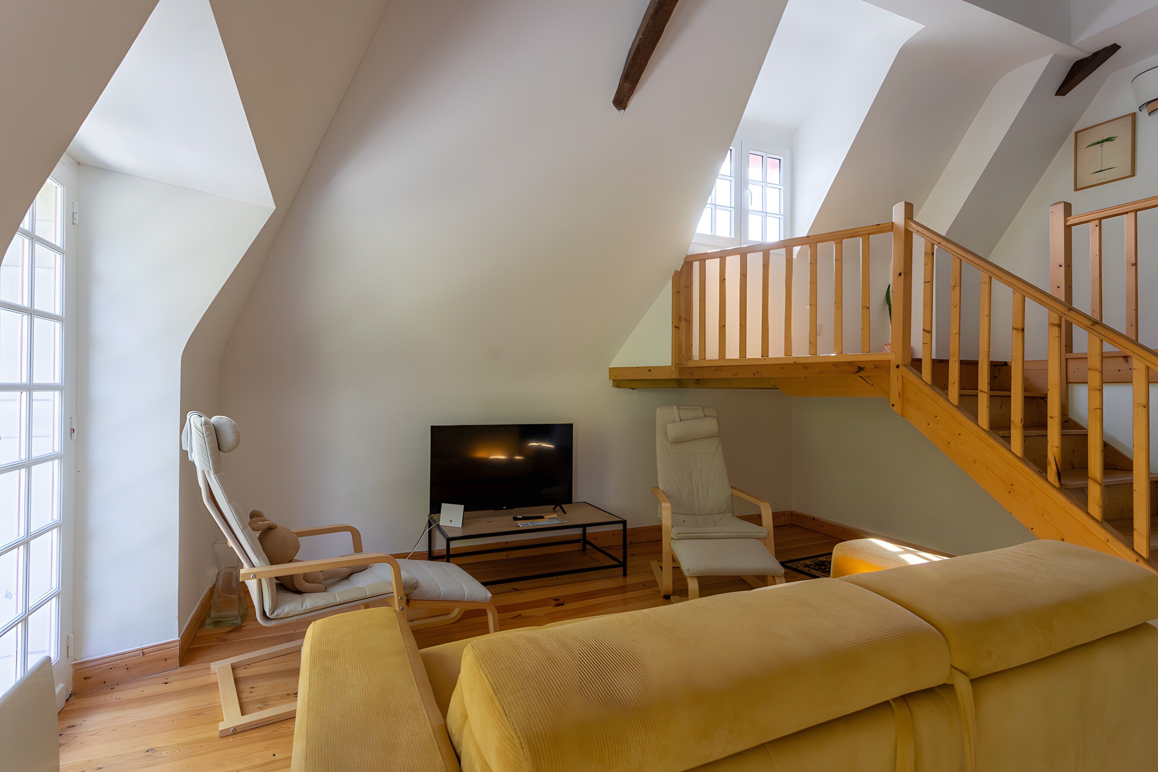 Una stanza in stile loft con una scala in legno, una TV a schermo piatto e un divano.