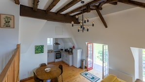 Un loft espacioso con vigas de madera a la vista, un comedor, una cocina y un ventanal grande.