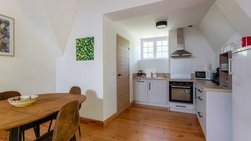 A compact kitchen with a dining table, chairs, a microwave, an oven, and a window.