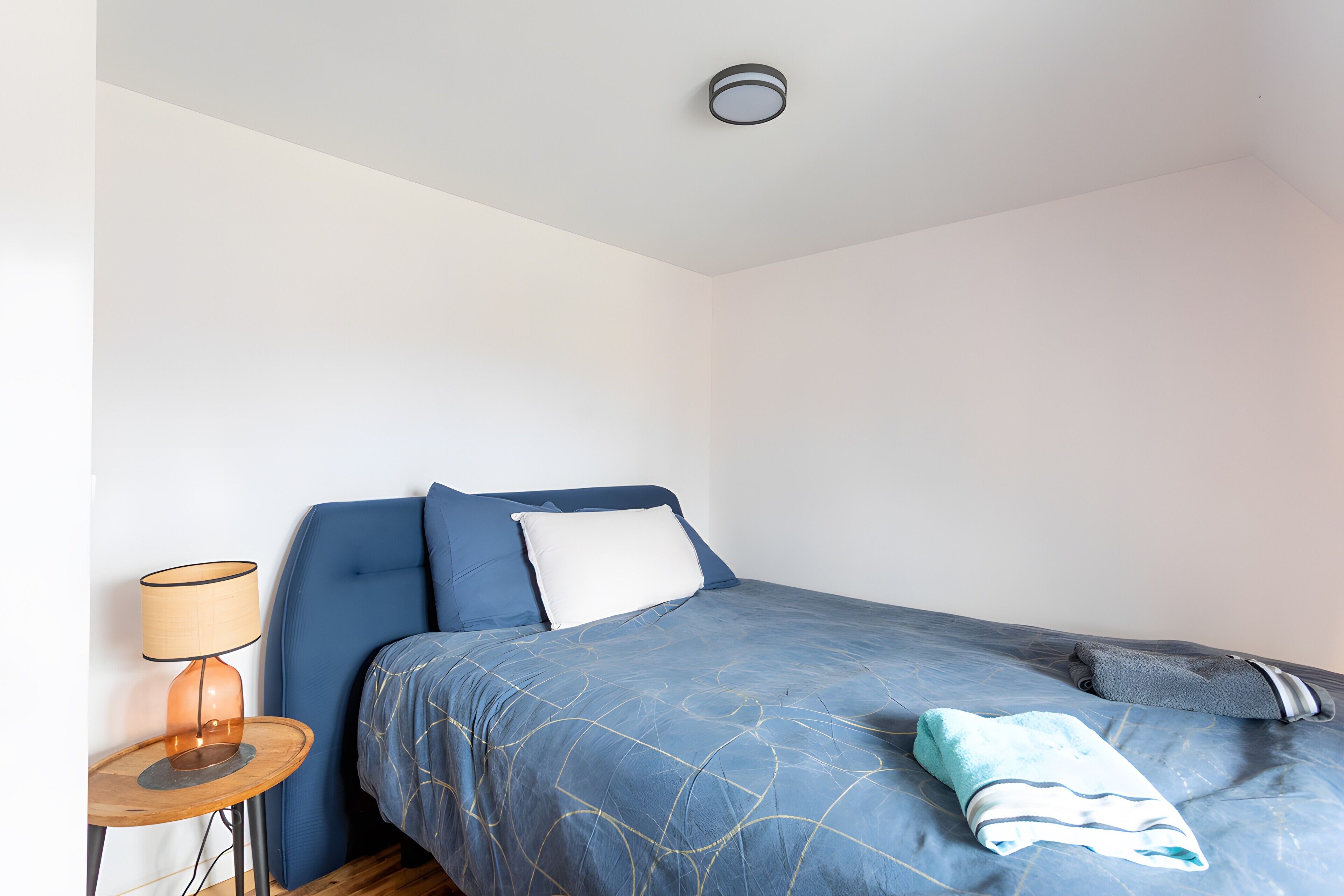 Une chambre à coucher avec un lit, une table de chevet avec une lampe et un luminaire au plafond.