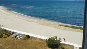 A beach view with a clear sky, a sandy shore, and a few people walking along the beach.
