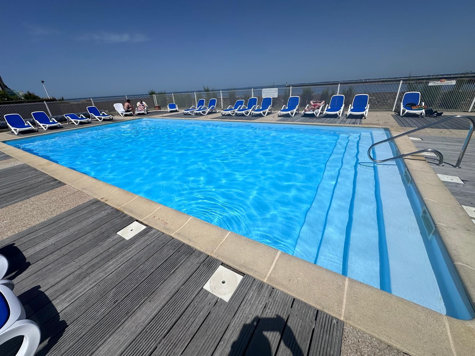A swimming pool with blue water, surrounded by blue lounge chairs and a wooden deck.