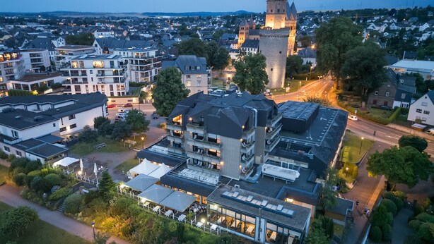 Vista aérea de un pueblo con una torre imponente de estilo castillo, edificios modernos y un espacio público bien cuidado con zonas de estar.