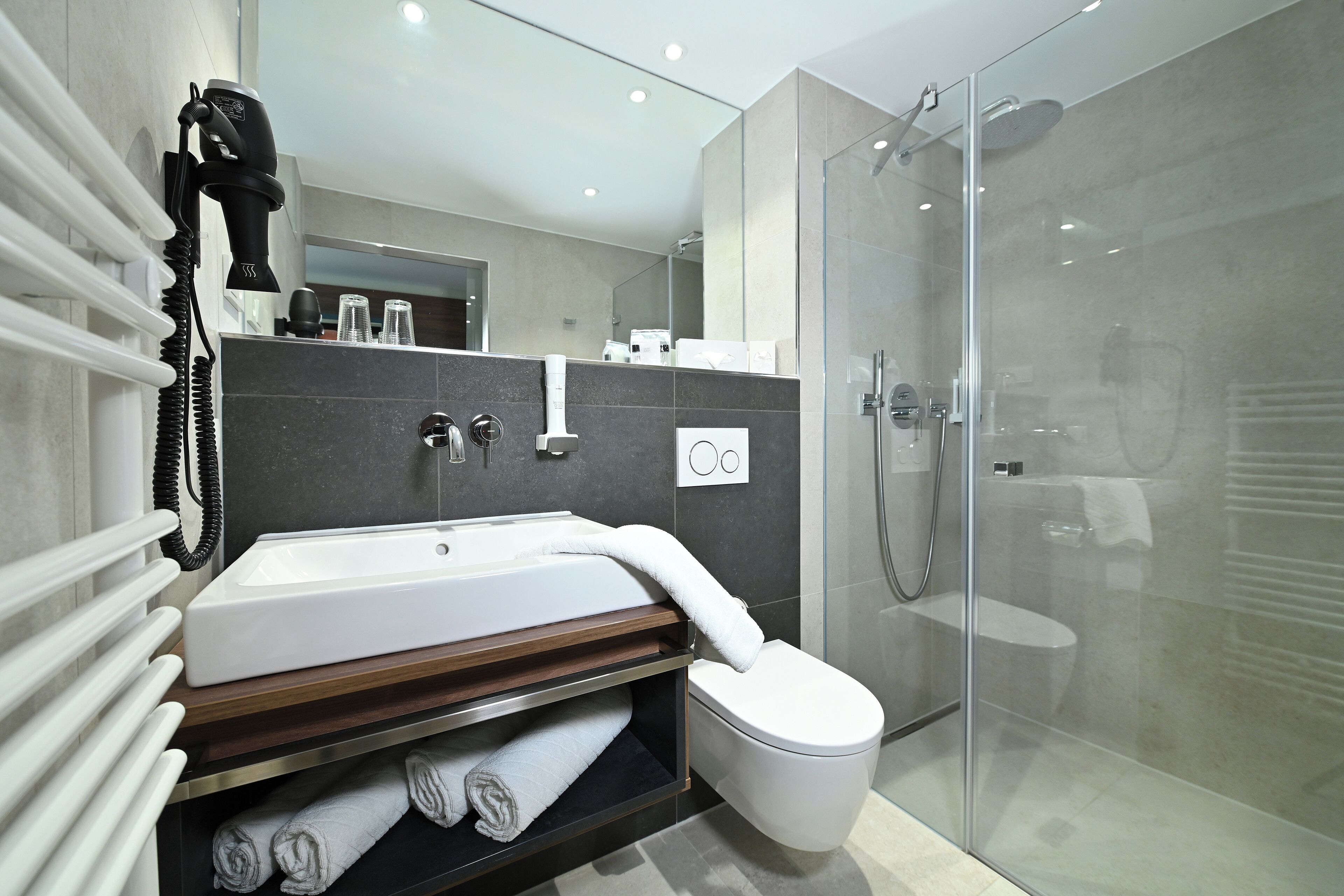 Een moderne badkamer met een glazen douchecabine, een wit wastafelmeubel en een handdoekrek.