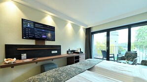 Habitación de hotel con una cama grande, un escritorio con computadora, una silla y un balcón con vista a una torre.