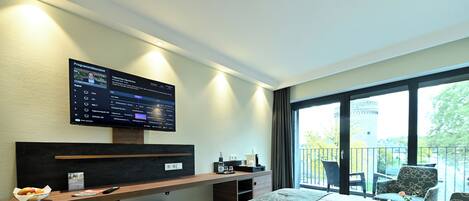 A hotel room with a large bed, a desk with a computer, a chair, and a balcony with a view of a tower.