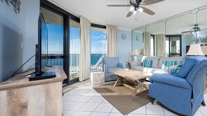 A modern living room with a balcony, a television, and a sofa. - Phoenix Vi 61004 2 Bedroom Condo (Orange Beach)