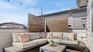 A modern outdoor seating area with a sofa, a coffee table, and a patterned rug. - Rams Roost Rooftop Hot Tub, Patio & Family Fun (Fort Collins)