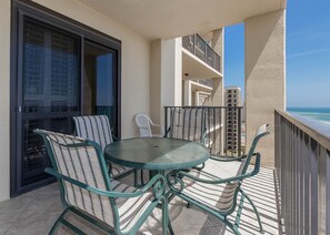 A balcony with a round table and chairs, a sliding glass door, and a view of the ocean and other buildings. - Phoenix Vi 61103 3 Bedroom Condo (Orange Beach)