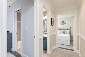A hallway leading to a bedroom with a bed, a dresser, and a mirror. - Phoenix Vi 61103 3 Bedroom Condo (Orange Beach)