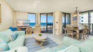 A living room with a TV, sofa, coffee table, and a balcony with a view of the beach.