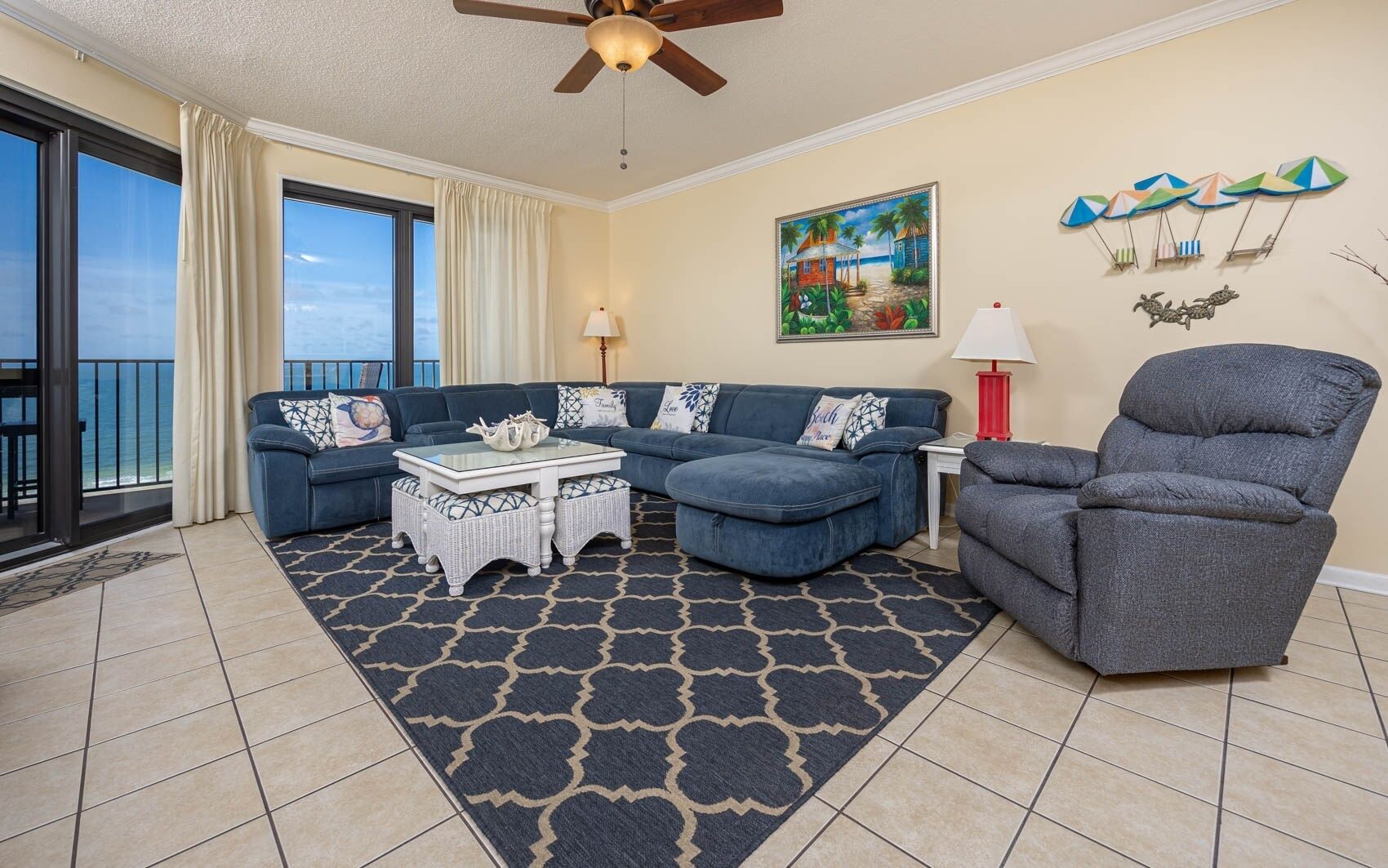 A living room with a blue sofa, a grey armchair, a patterned rug, and a painting of a beach scene.